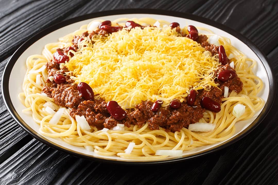 A Cincinnati chili spaghetti with meat, beans, onions, and cheese served in a plate.